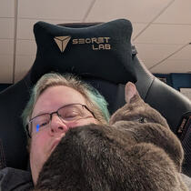 A selfie of me in my chair, with a grey cat nuzzling me that is sitting on my chest.